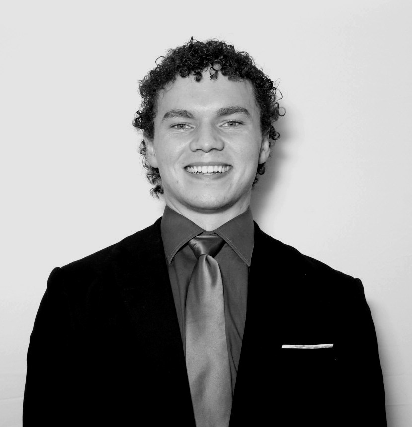 Black and white headshot of Ethan Lewis smiling, in a dark suit and tie